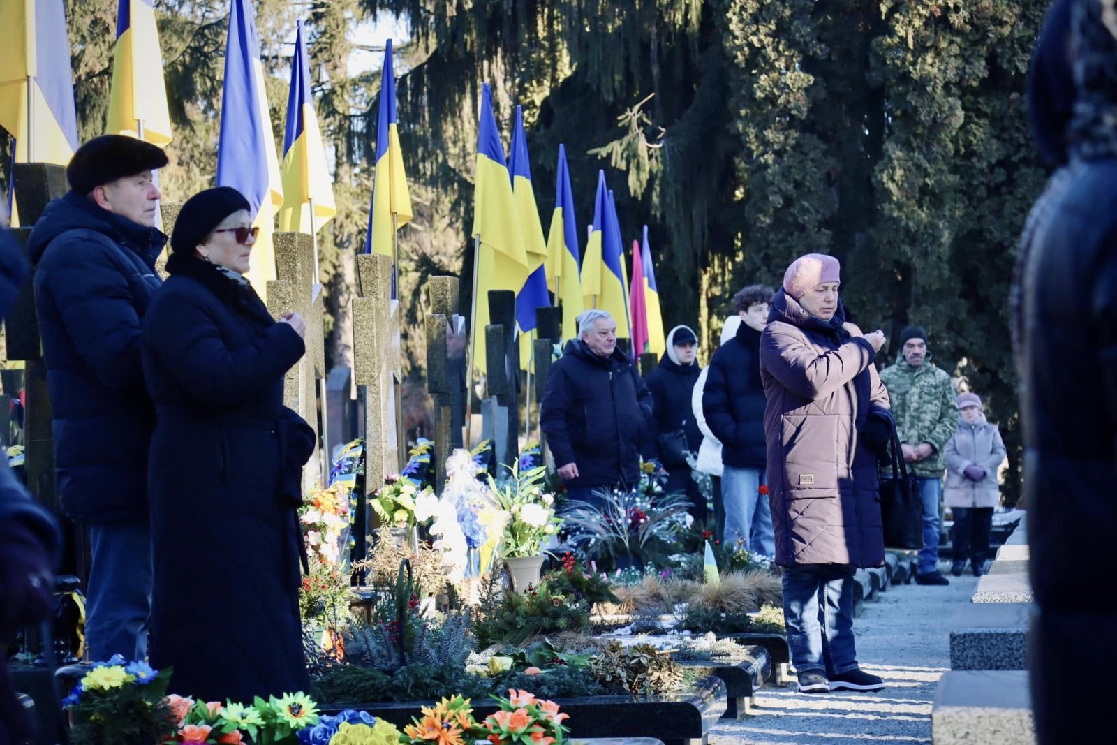 Люди стоять на кладовищі, біля могил полеглих воїнів.
